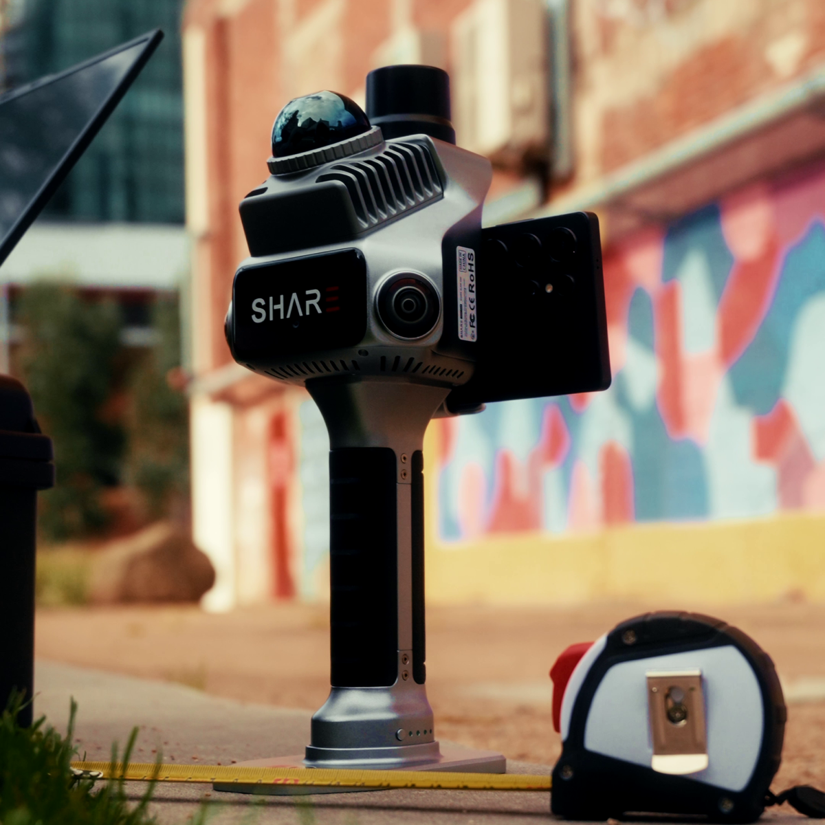 SHARE C1 Pro standing outdoors with a phone mounted, beside a tape measure